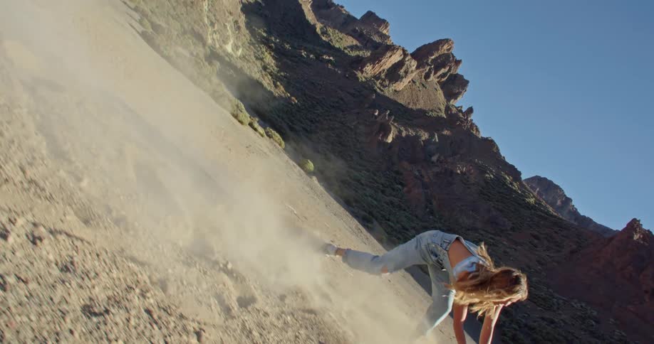 A woman playing in sand with a stick with a cliff the sky and clouds in the background