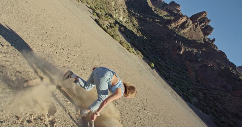 Blonde woman with strappy denim jumpsuitdraws shapes on the ground in valley