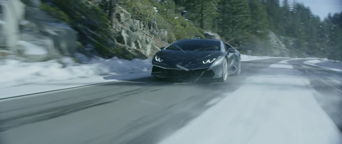 A metallic black car driving down a snowy road