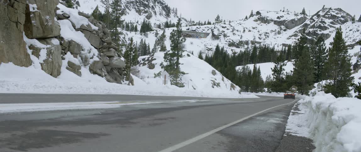 A black car speeds down a mountain road in the winter