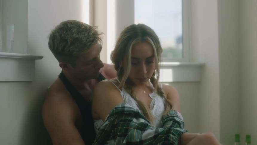 A man leans into his girlfriends neck as she sits in his lap on the floor of a downtown apartment