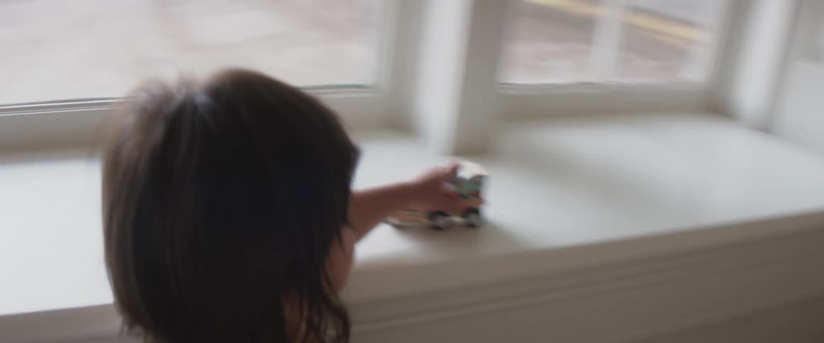 A  child at home plays with a toy car on a window ledge