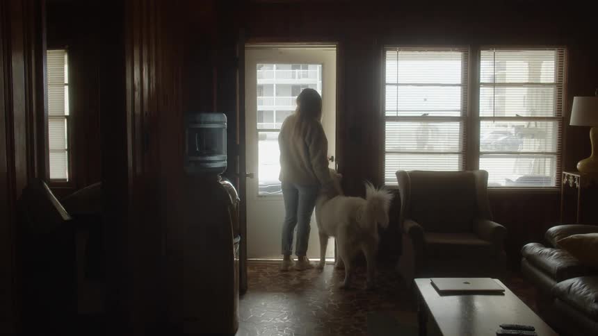 A woman walks through a living room with her dog behind her and opens the door and they both go outside