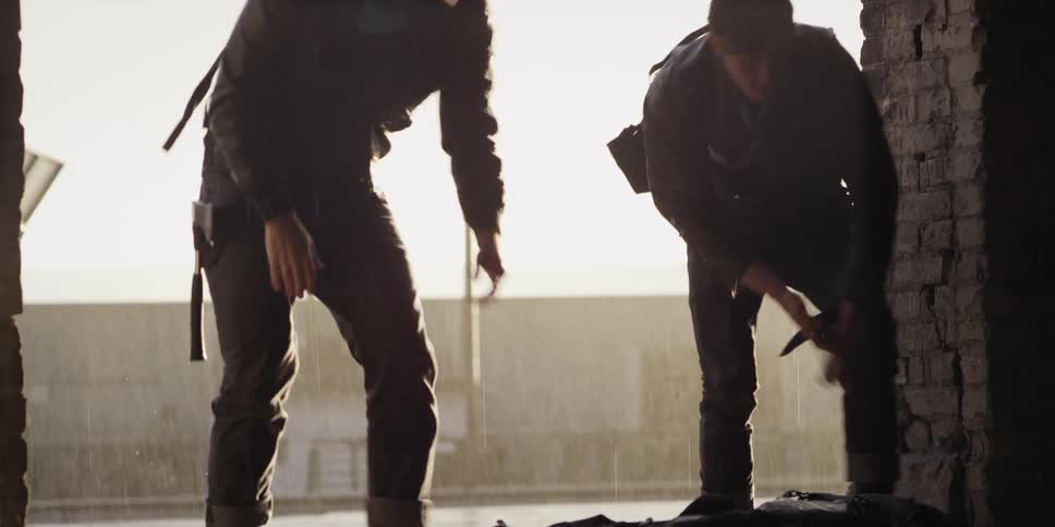 Two young men carrying duffel bags enter a warehouse on a rainy morning