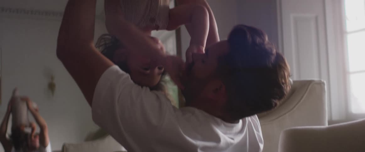 A father in a room playing with a child with a mirror a wall and window in the background