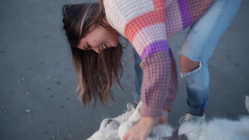 Young woman wearing colorful sweater cuddling a dog on the floor at evening