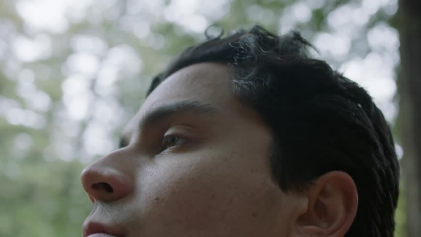 Close up of the face of a young man looking around the forest