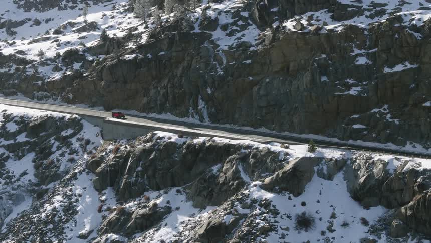 Aerial view of a red car driving on a road throught the snow covered mountain