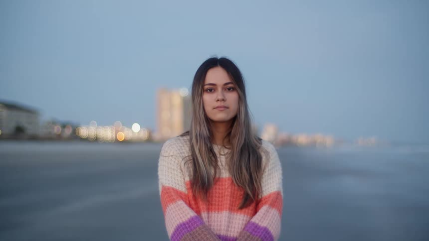 A woman is standing still with a coastal city and body of water as her backdrop