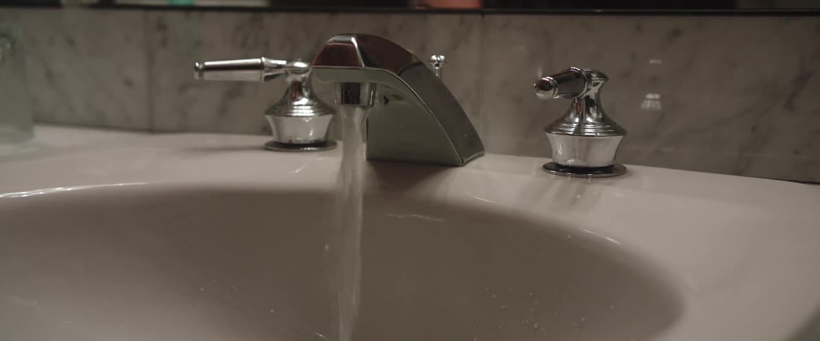 Person turns on bathroom sink faucet and fills water glass then sets down empty glass