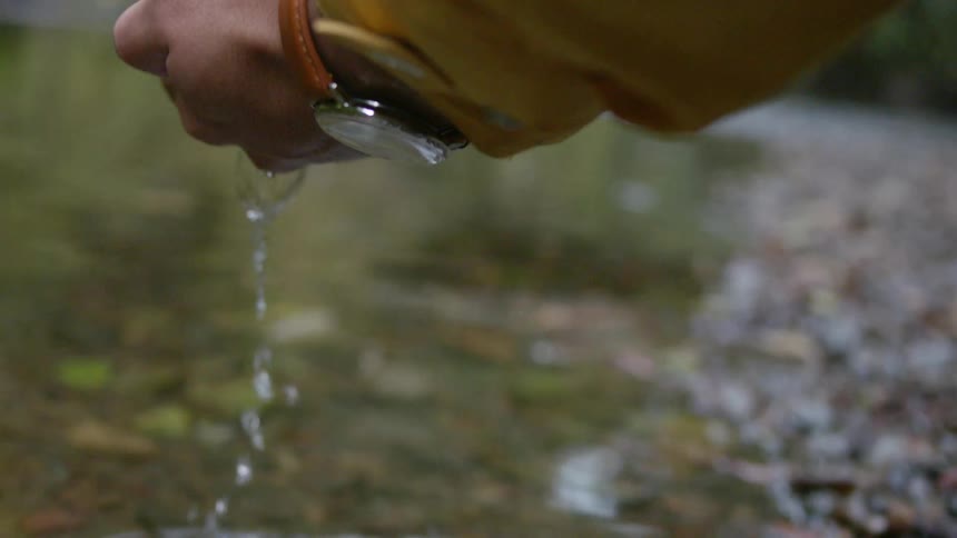 A man is scooping up water from a river then lets it fall from his hand