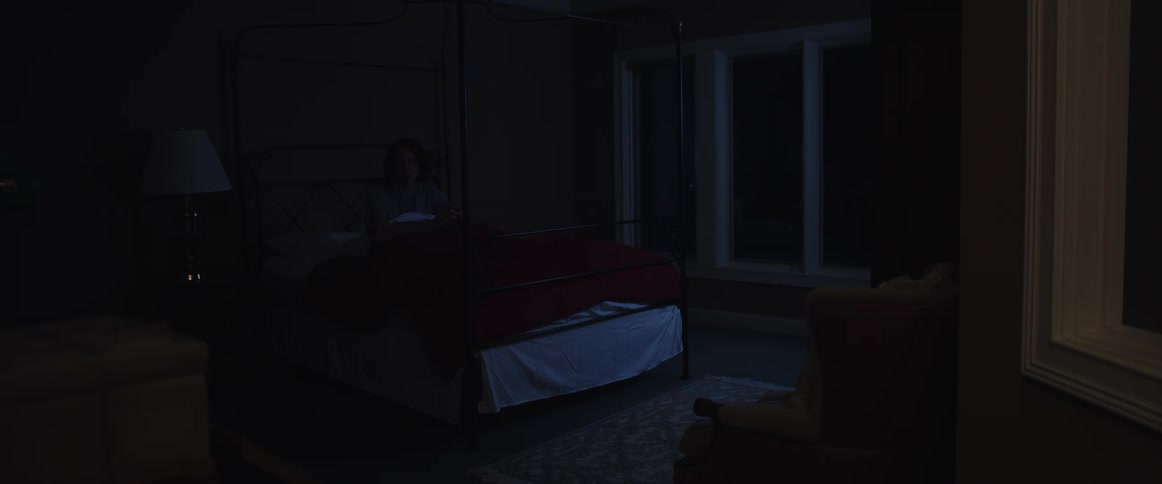 A man in bed wakes up and turns on the light then walks through the room