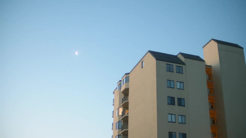 The moon shines in the sky above a building with many windows and patios