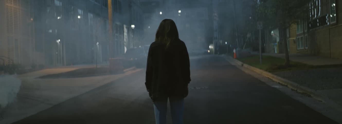 Silhouette of a hooded person standing on a foggy street in the city at night
