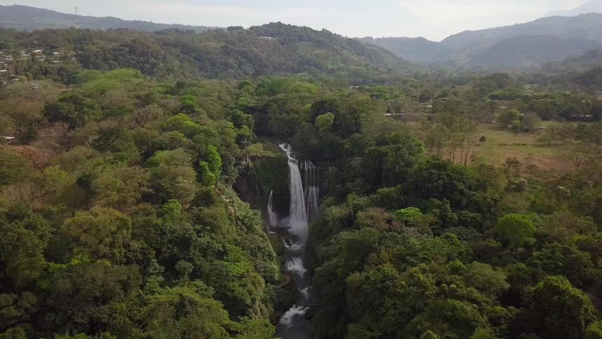 Aerial view of a waterfall flowing on between the trees in the mountain