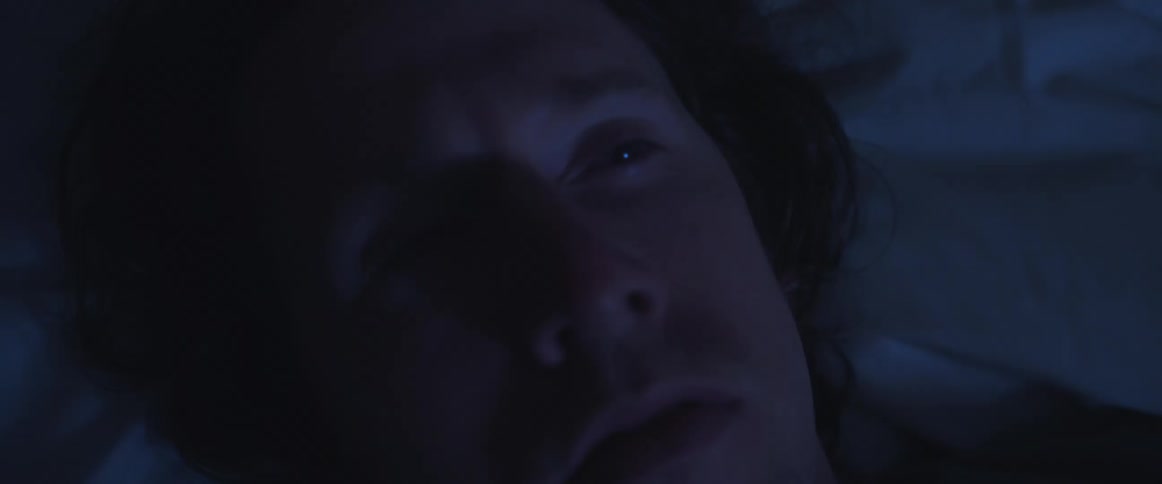 Man with long hair lies down on bed opens his eyes in fear in the darkness