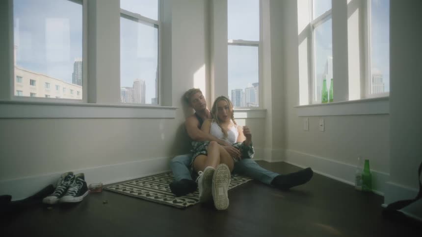 A girl sitting on the floor between her boyfriends legs while he naps