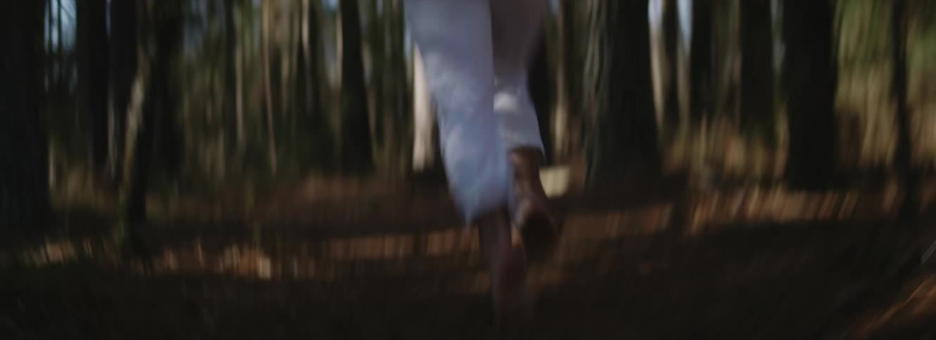 A person running in a forest with trees with the sky and clouds in the background