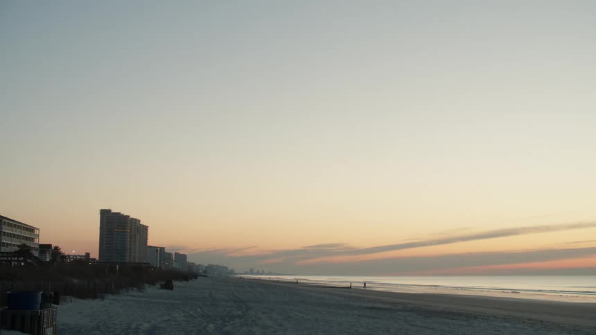 Buildings of a waterfront city in front of a deserted lonely beach near the ocean at sunset