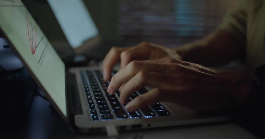 A man sits and types on a laptop