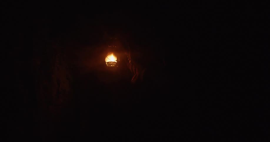 A person stands in a dark cave by a light on the wall