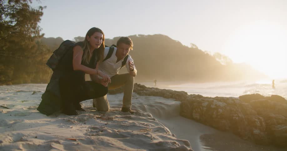 Young couple kneeling in front of the beach close to the ocean at sunset