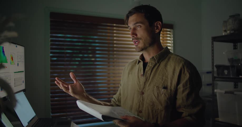 A man in a room with a notepad talking to a computer with a wall and window in the background