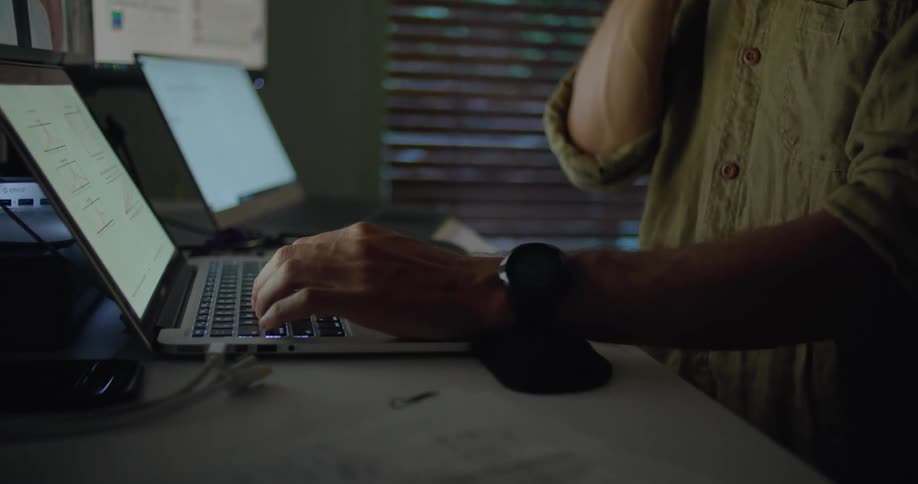 A man is working in a home office in the evening using two laptop computers