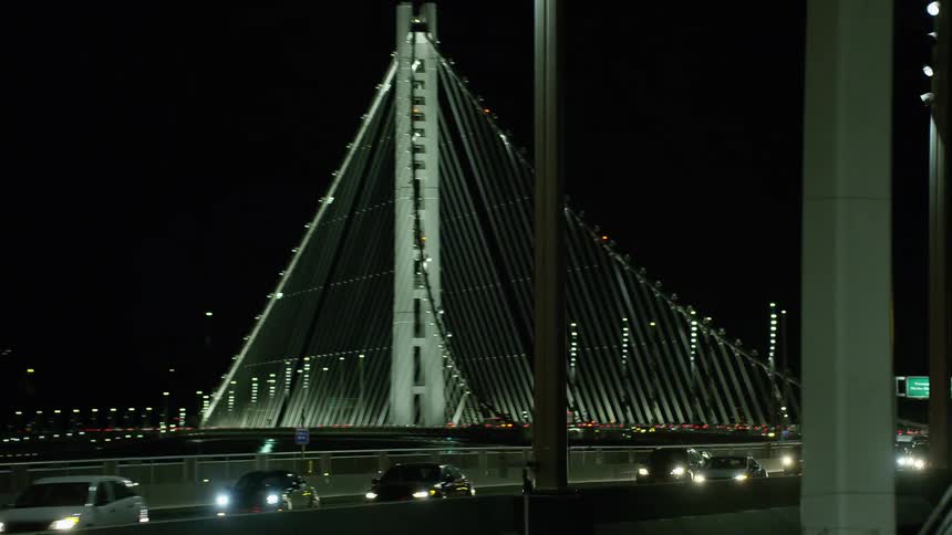 Traffic travels across a large suspension bridge in a city at night