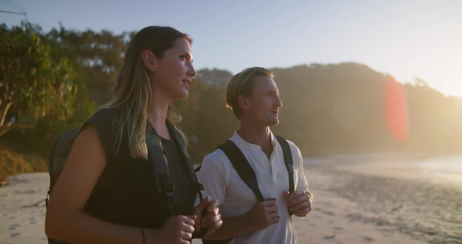 A man and woman wearing backpacks look out over the ocean