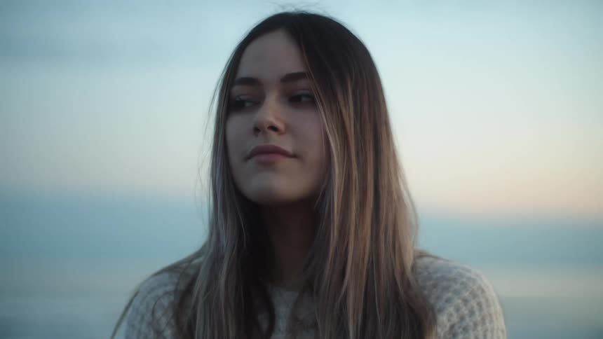 Long haired blonde young woman stands looking at the horizon at sunset