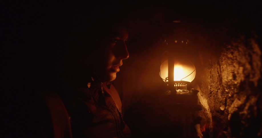 A man holds up a lamp as he touches the wall of a cave in awe