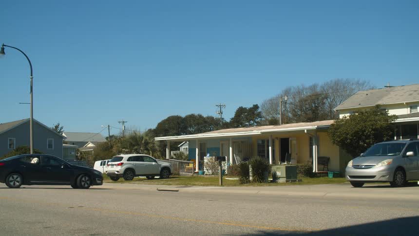 A vehicle reversing from a house and driving on a road with the sky and clouds in the background
