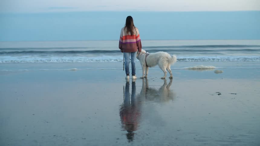 Young woman wearing a colorful sweater stands with in front of the ocean