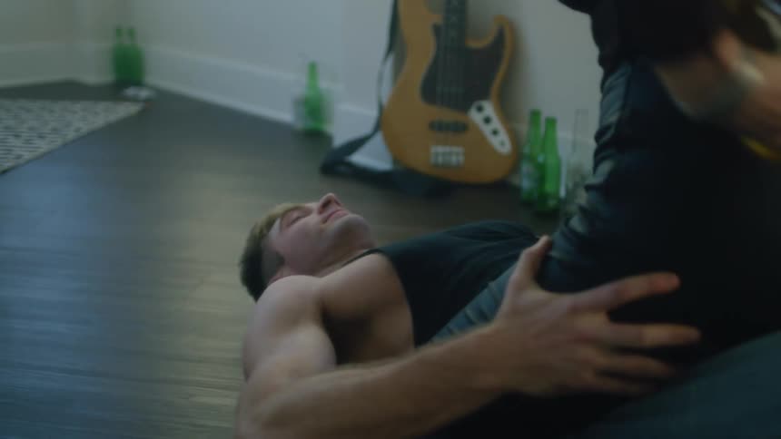 Young muscular man lays down on the floor while someone sits over him pouring beer on his face