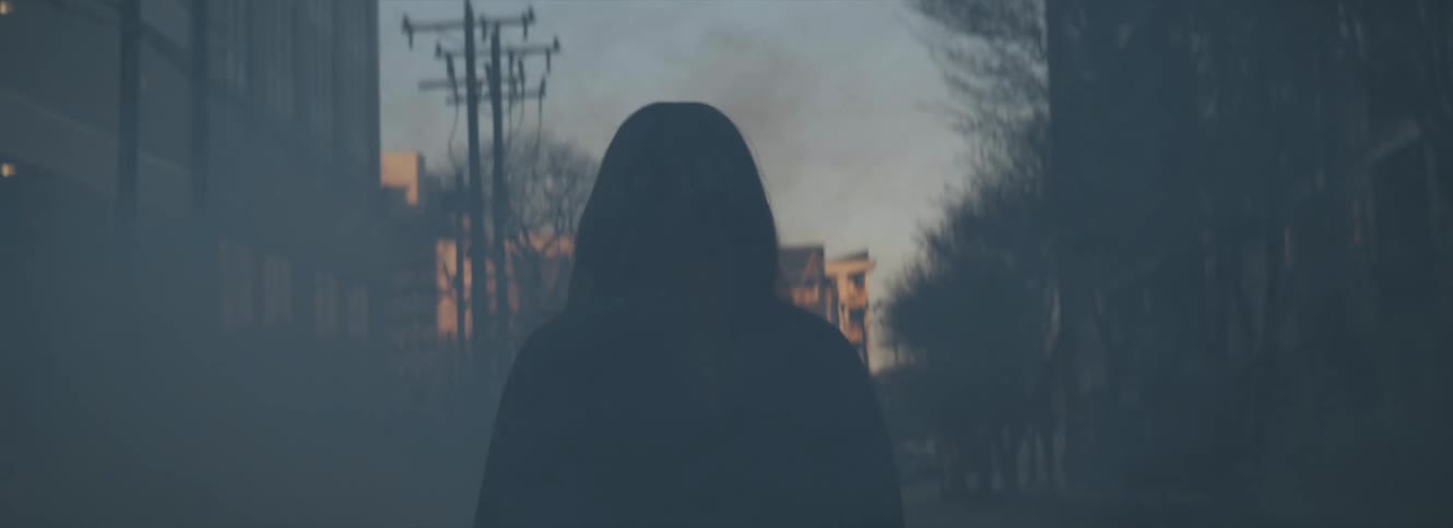A woman walks down a smoke filled street in a city