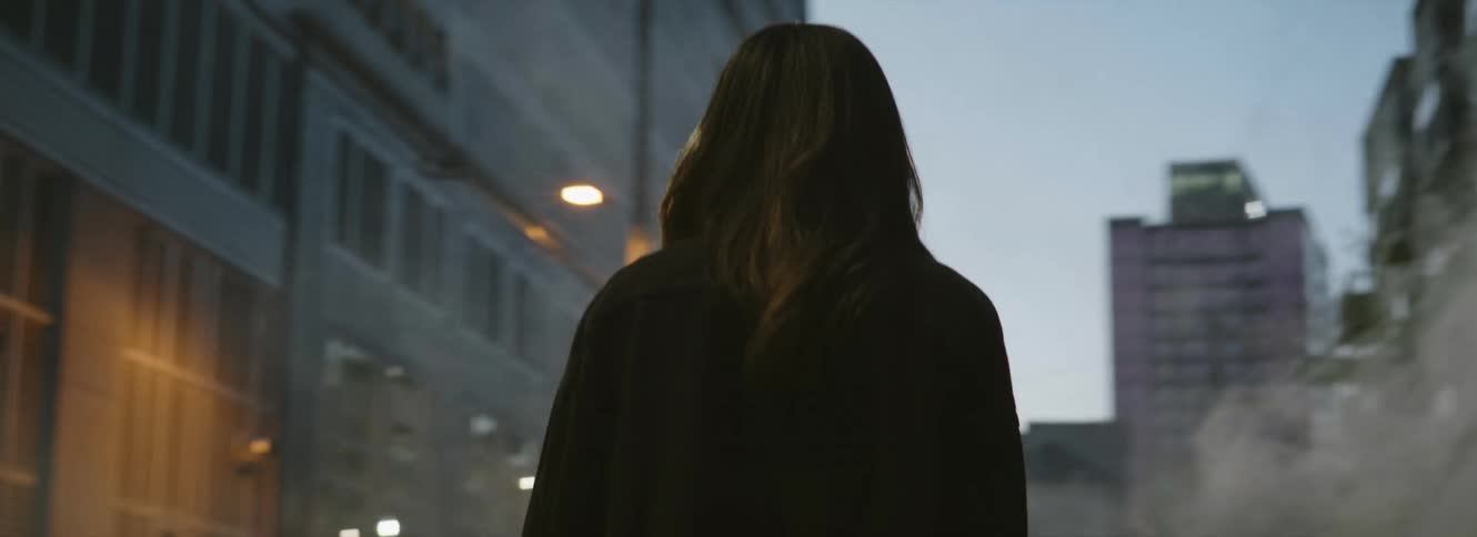 A woman is standing on a city street looking at smoke coming from a building