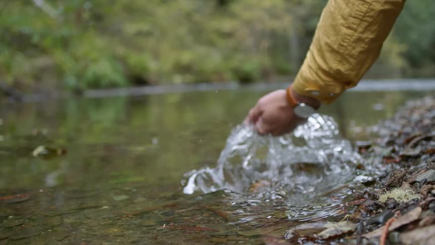 A person with a wristwatch using their hand to scoop water from a stream