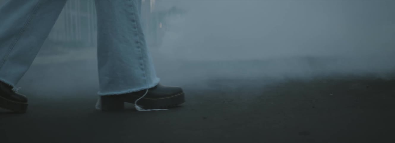 A person with jeans and shoes walking on a city street with smoke