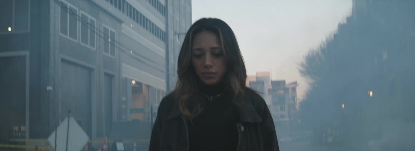 Woman walks along street pass building through smoke