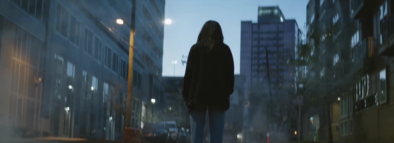 A person is standing in a downtown city at dusk