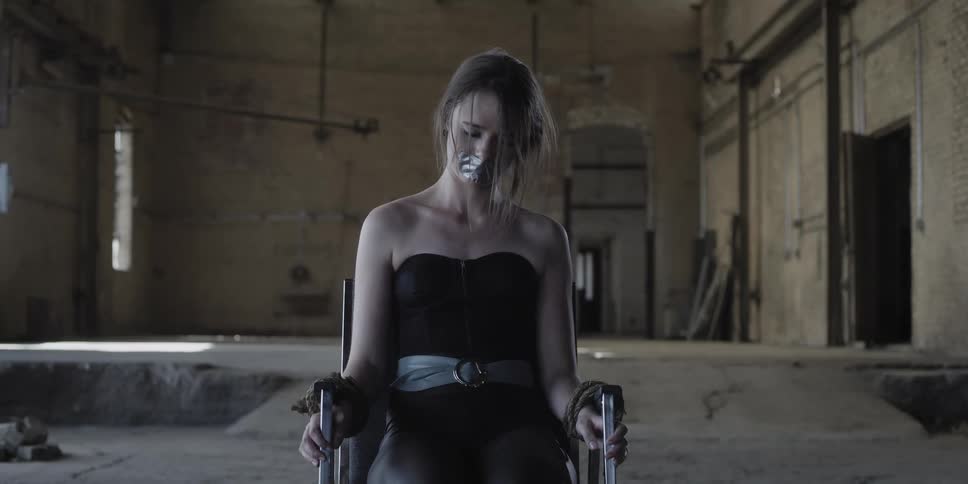 Young woman gagged and tied to a chair inside an abandoned warehouse