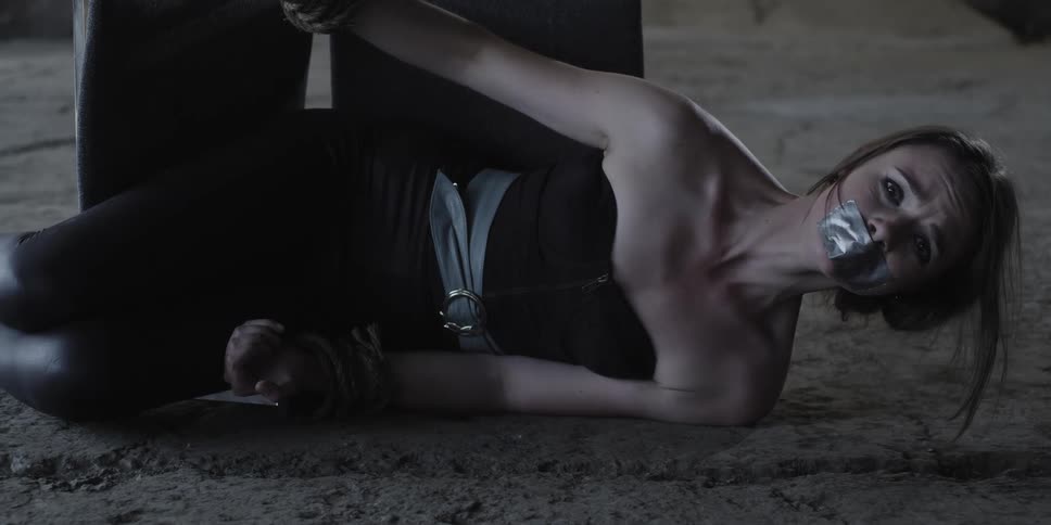 A gagged and bound woman is laying on her side with the chair knocked over