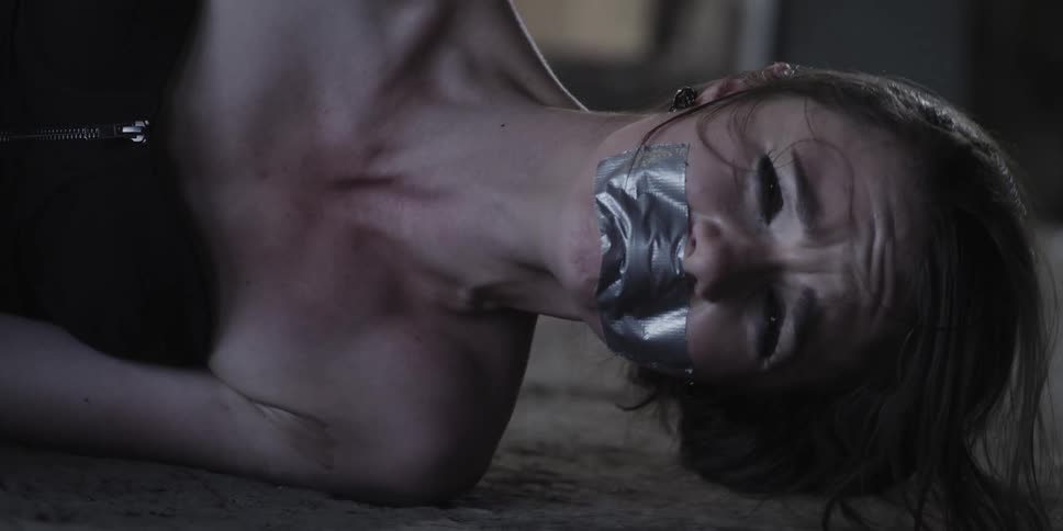 Nervous crying woman lays on the floor of an abandoned warehouse tied up and gagged