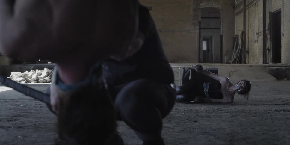 A woman is tied to a tipped over chair while one man threatens another tied up man with an ax