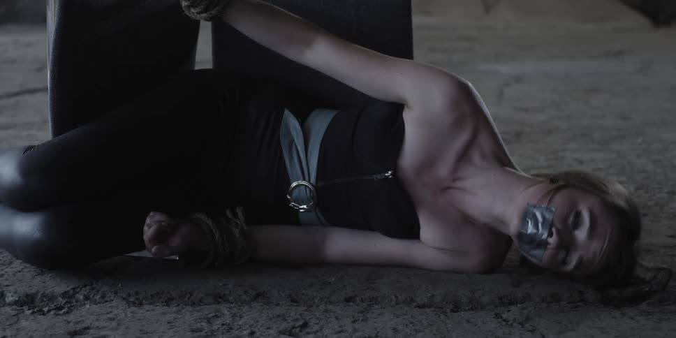 Scared woman gagged and tied to a chair laying on the floor of a warehouse