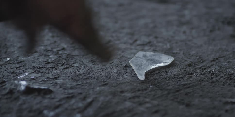 A man waves his hand towards a broken piece of glass on the ground