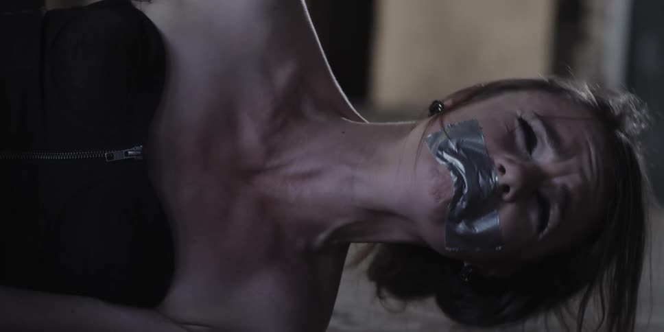 Fearful distressed woman lays on the floor of an abandoned warehouse with tape over her mouth