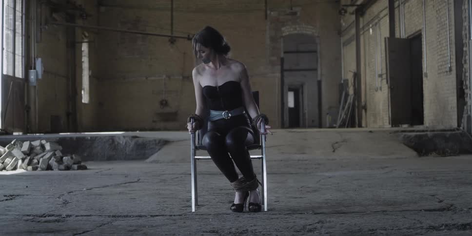 A woman sobs while trying to escape from being tied in a chair in a run down building
