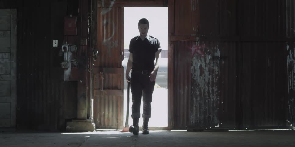 A man in a room walking with an ax with a wall and doorway in the background